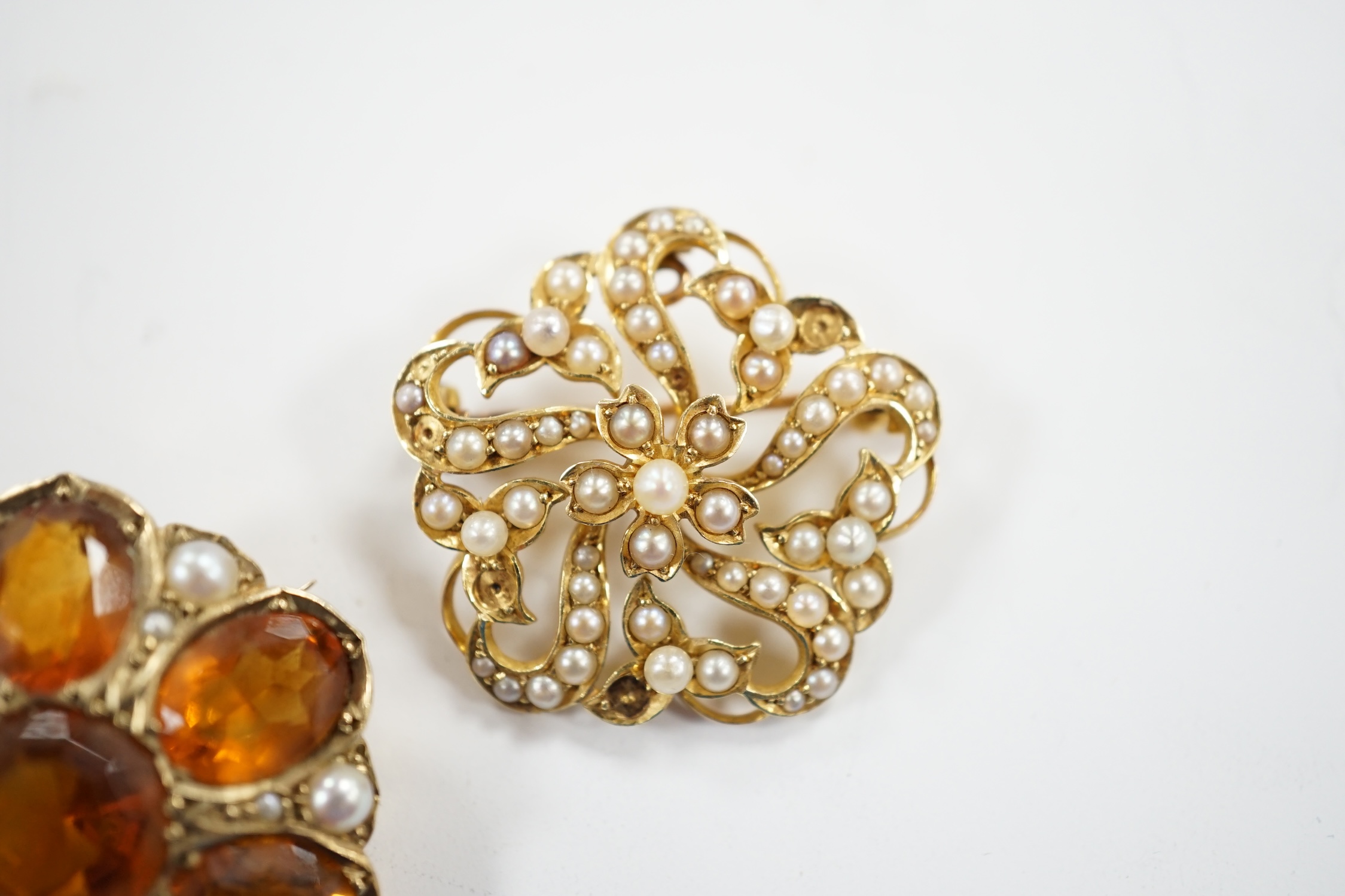 An early 20th century yellow metal, citrine and split pearl cluster set shaped circular brooch, 28mm and a similar 15ct and seed pearl cluster set brooch, gross weight 18.5 grams.